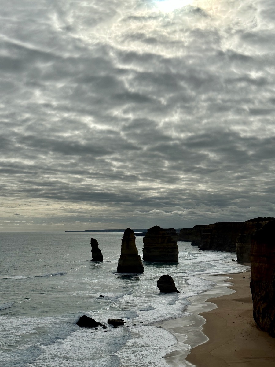 Majestic limestone stacks rise from the ocean along Australia's iconic Great Ocean Road under a cloudy sky.